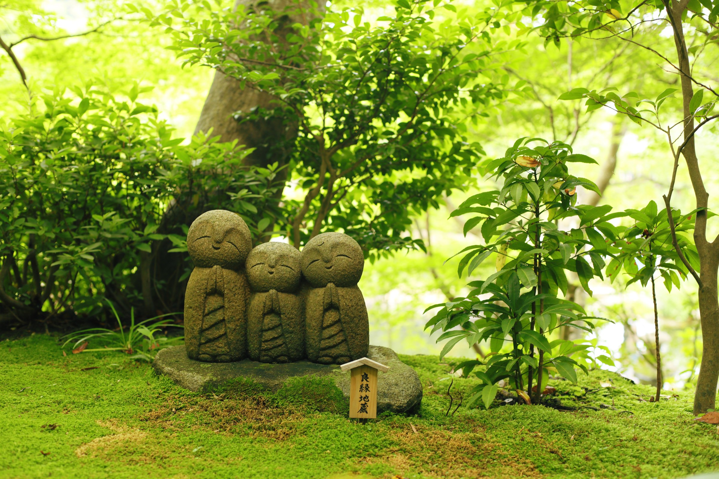 Three stone statues in a mossy green garden
